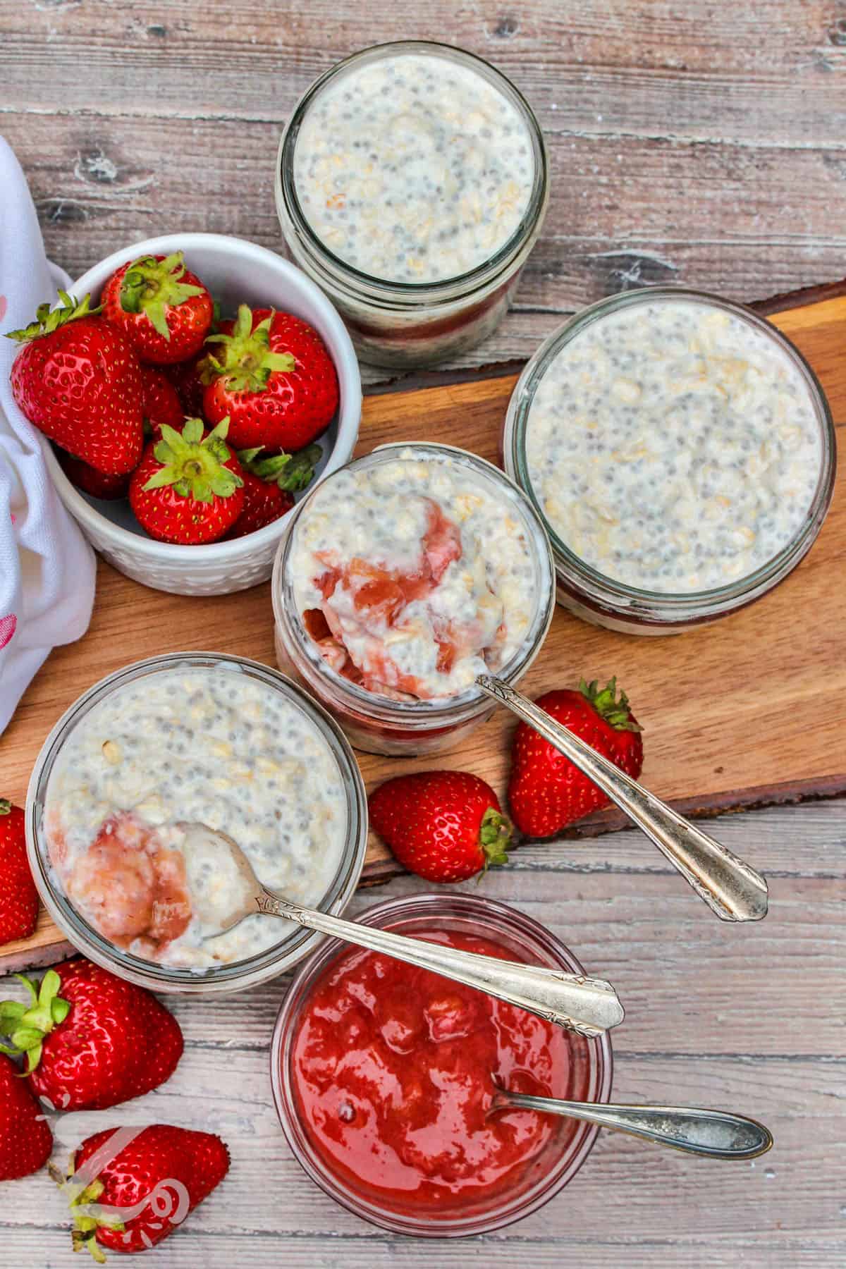 jars of Overnight Oats with spoons and a bowl of strawberries