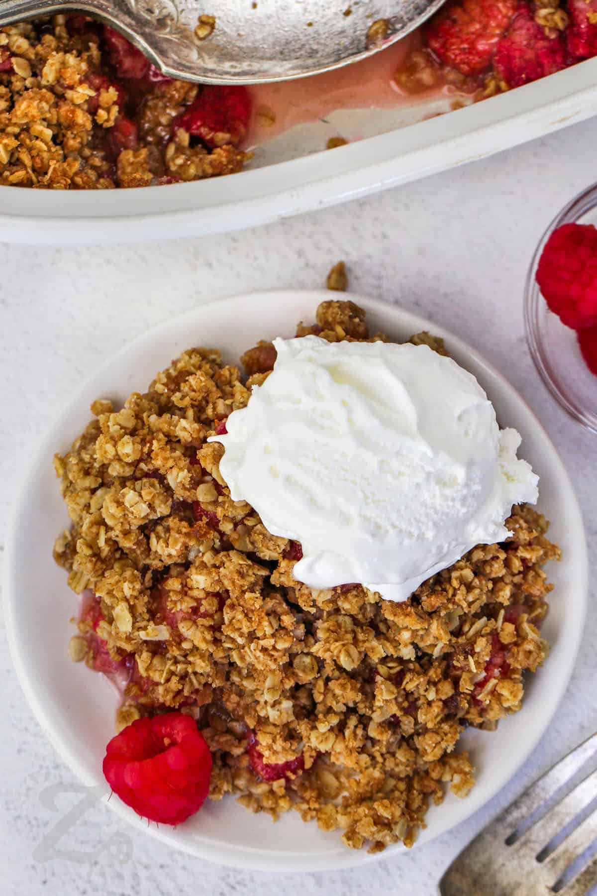 raspberry crisp with a scoop of vanilla ice cream on top, served on a small white plate, with more raspberry crisp in the background