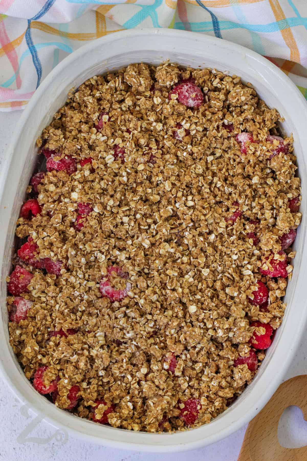 oat topping over raspberry mixture in a white baking dish to make raspberry crisp