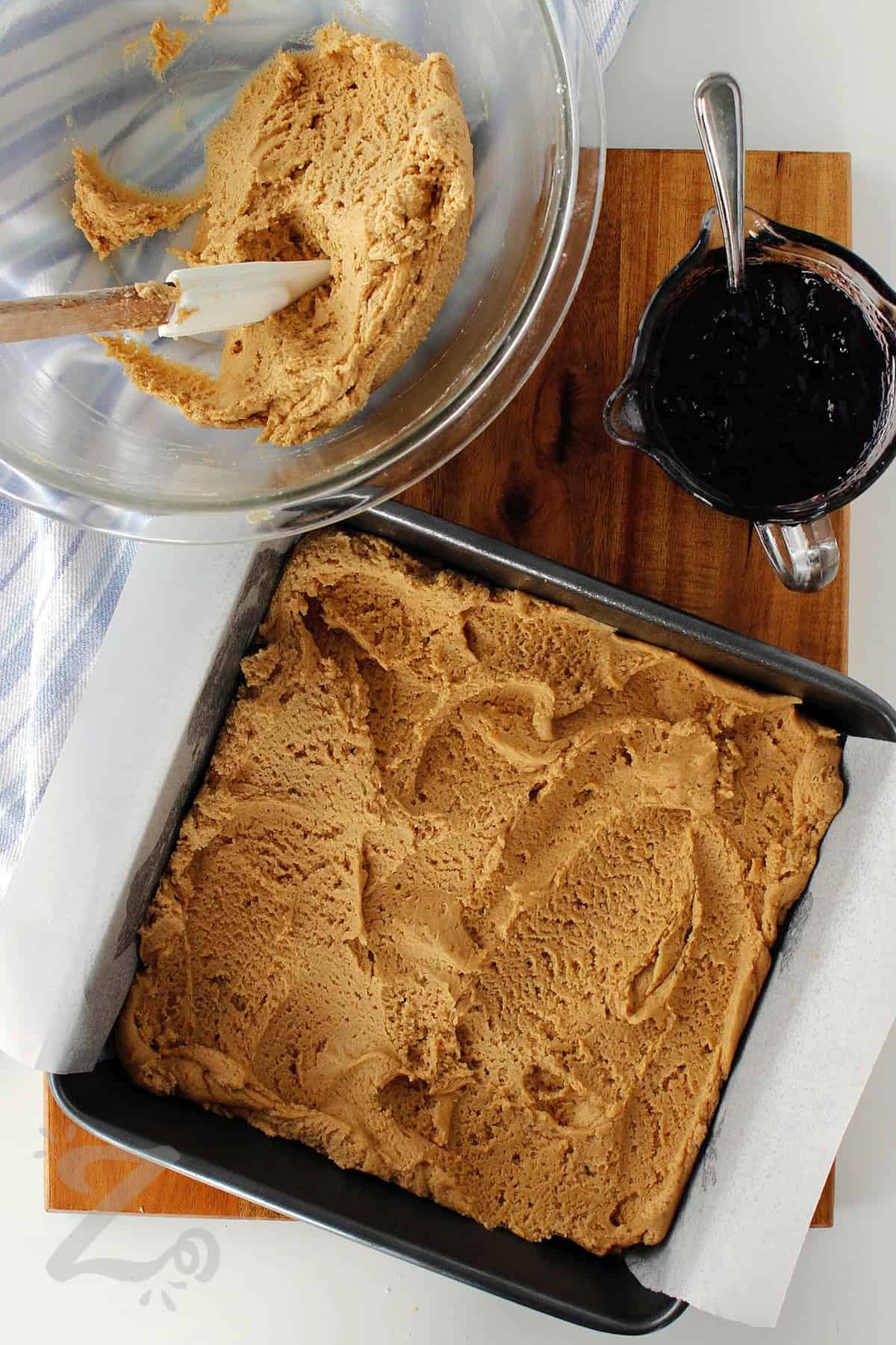 peanut butter dough spread in a parchment lined pan, leaving a bit remaining in the bowl, to make peanut butter and jelly bars