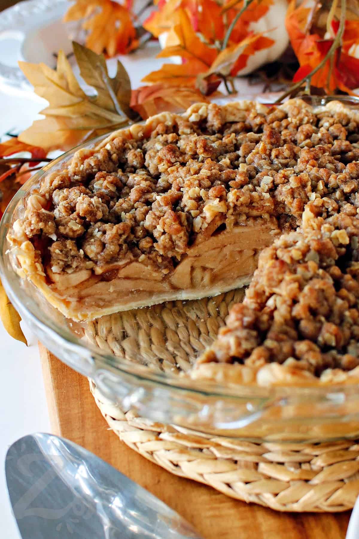 baked apple crumb pie in a clear pie plate with a slice taken out