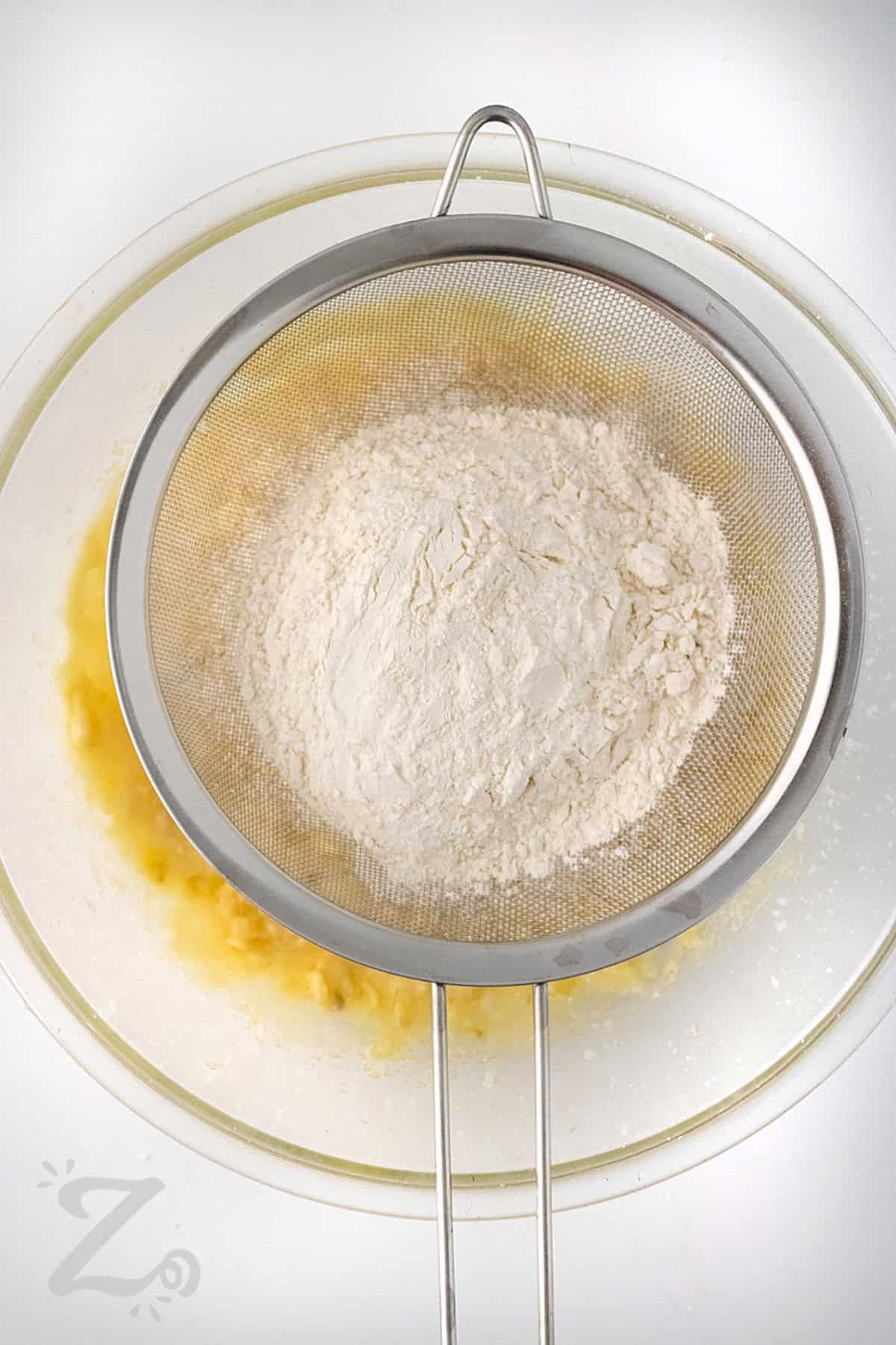 adding sifted flour to bowl to make Strawberry Banana Muffins