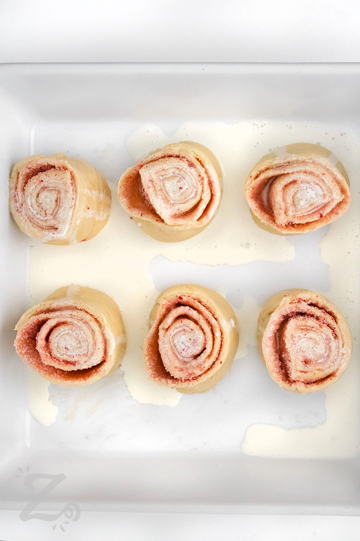 adding frosting to Strawberry Cinnamon Rolls before baking