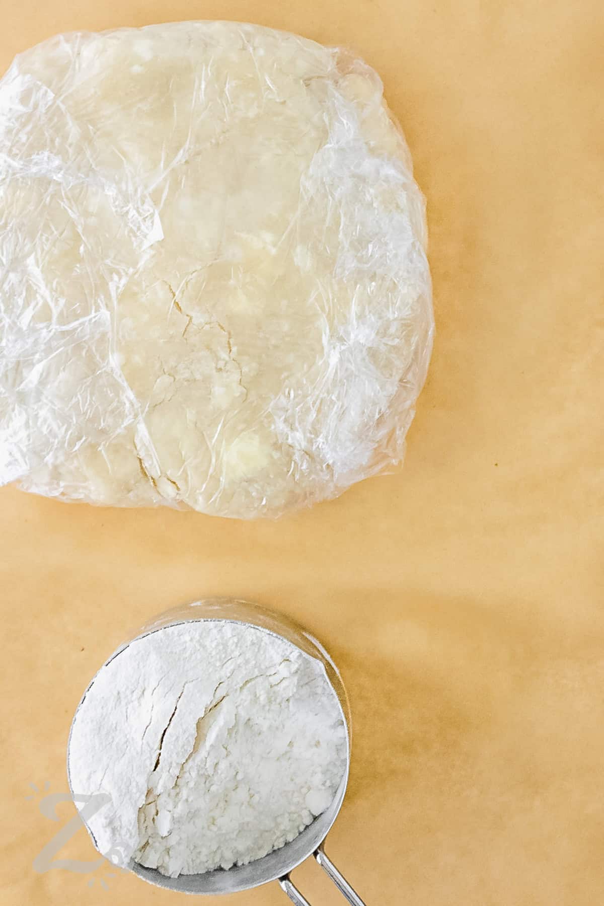 Easy Pie Crust dough in saran wrap and a measuring cup of flour