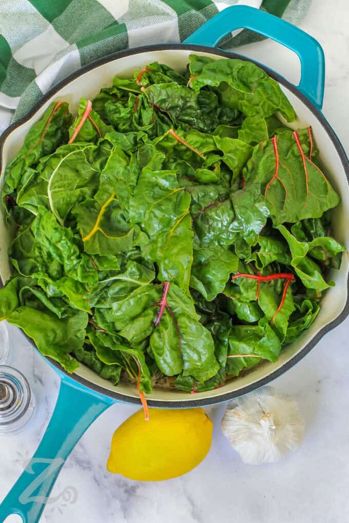 adding leafy greens to pan to make Swiss Chard