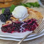a serving of blackberry pie on a plate topped with ice cream
