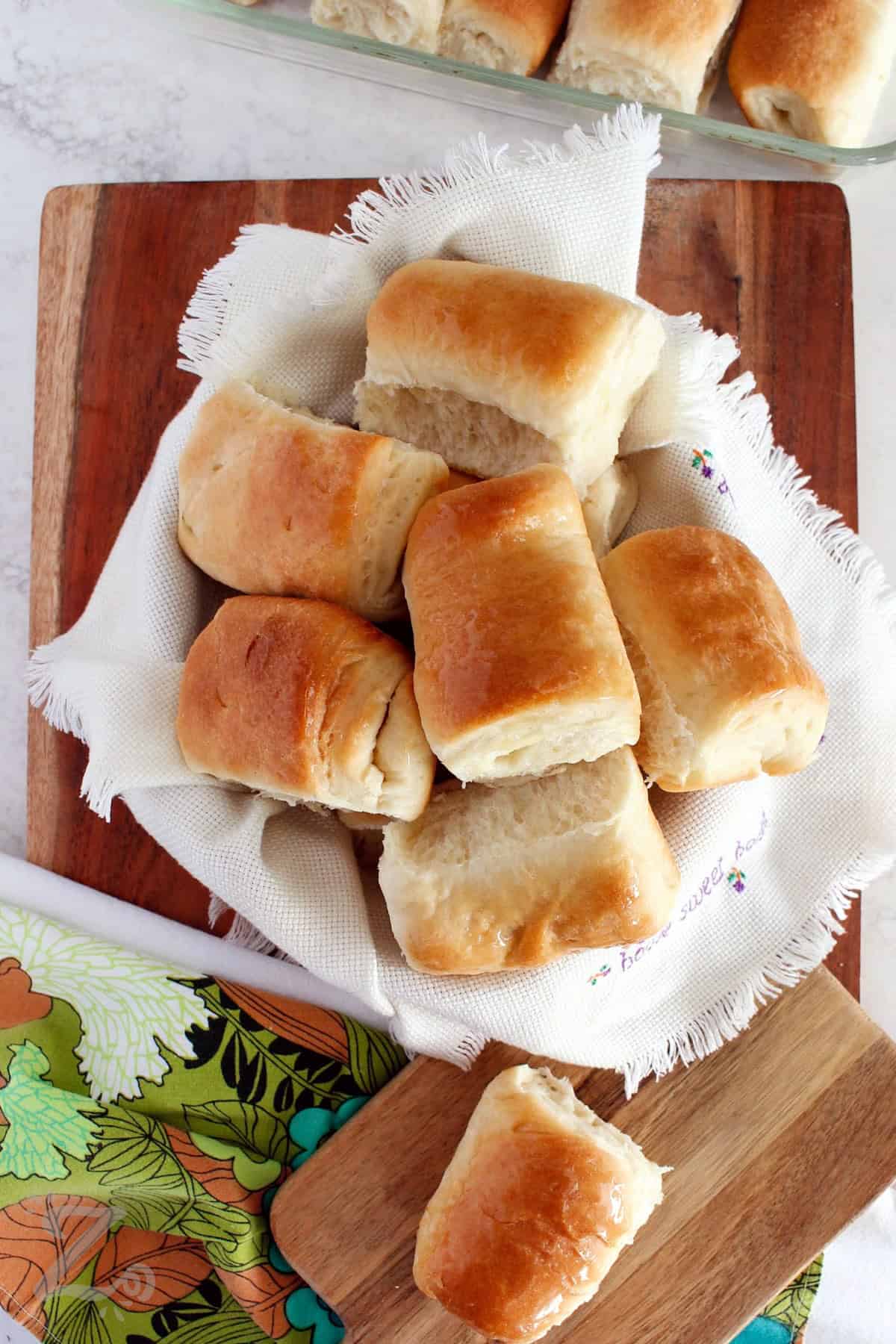 Parker House Rolls in a basket with one roll on the side, and more in the baking dish.