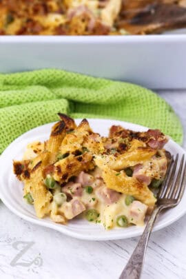 Ham and pea pasta on a plate in the foreground, with a casserole dish in the background.