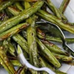 roasted green beans on a plate with serving utensils