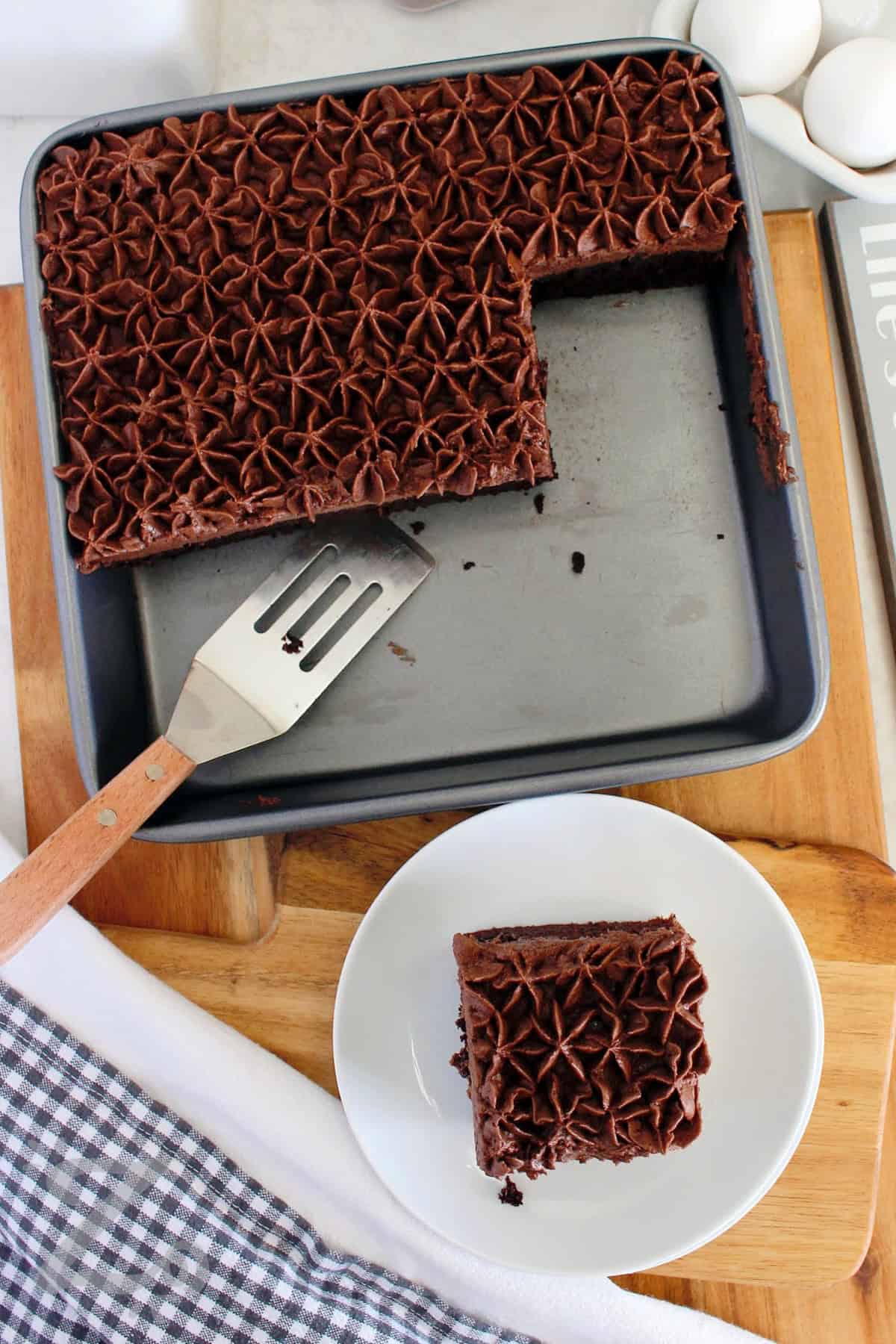 Rich, moist, and deeply chocolatey, this homemade chocolate cake recipe is quick to prepare and always a hit. Whether you frost it for celebrations or serve it plain, it’s a classic dessert you’ll come back to again and again. Try it tonight for a casual dessert. #ourzestylife slice of homemade chocolate cake on a white plate, with remaining cake in a square baking pan beside it