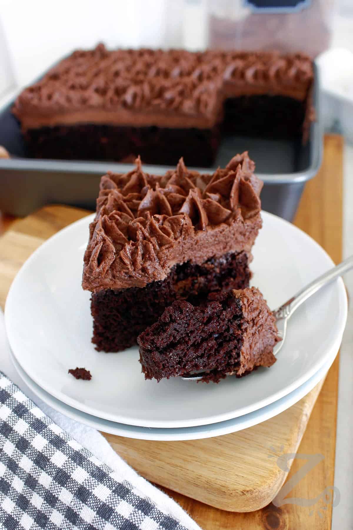 Homemade chocolate cake is a soft, moist, and deeply chocolatey cake that proves homemade baking doesn’t need to be complicated. This recipe is simple to follow and delivers consistent, delicious results every time you bake it. This scratch recipe is perfect for celebrations or just a simple weeknight dessert so why not give it a try? #ourzestylife a slice of homemade chocolate cake on a white plate with a forkful in the front of the cake