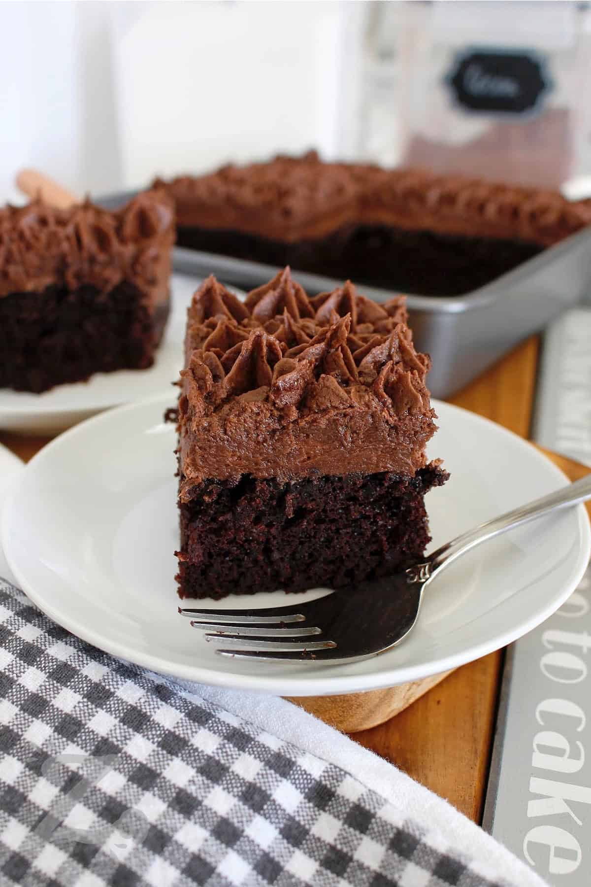 This easy homemade chocolate cake recipe is made with everyday pantry staples and bakes into a soft, moist, and flavorful dessert. It’s simple and reliable so why not bake it for your next special occasion or casual dinner? #ourzestylife a slice of homemade chocolate cake on a white plate with a fork