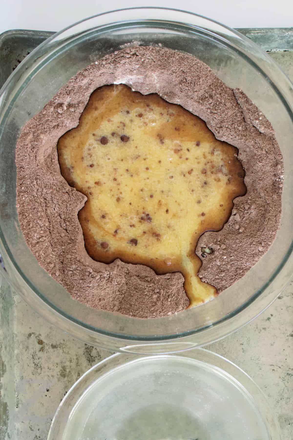 A rich and fluffy homemade chocolate cake that’s easy enough for beginners but delicious enough for any celebration. Each slice is soft, moist, and full of deep cocoa flavor, making it the perfect dessert for any occasion. Why not give this recipe a try? #ourzestylife process to make homemade chocolate cake where wet ingredients are added to the dry ingredients