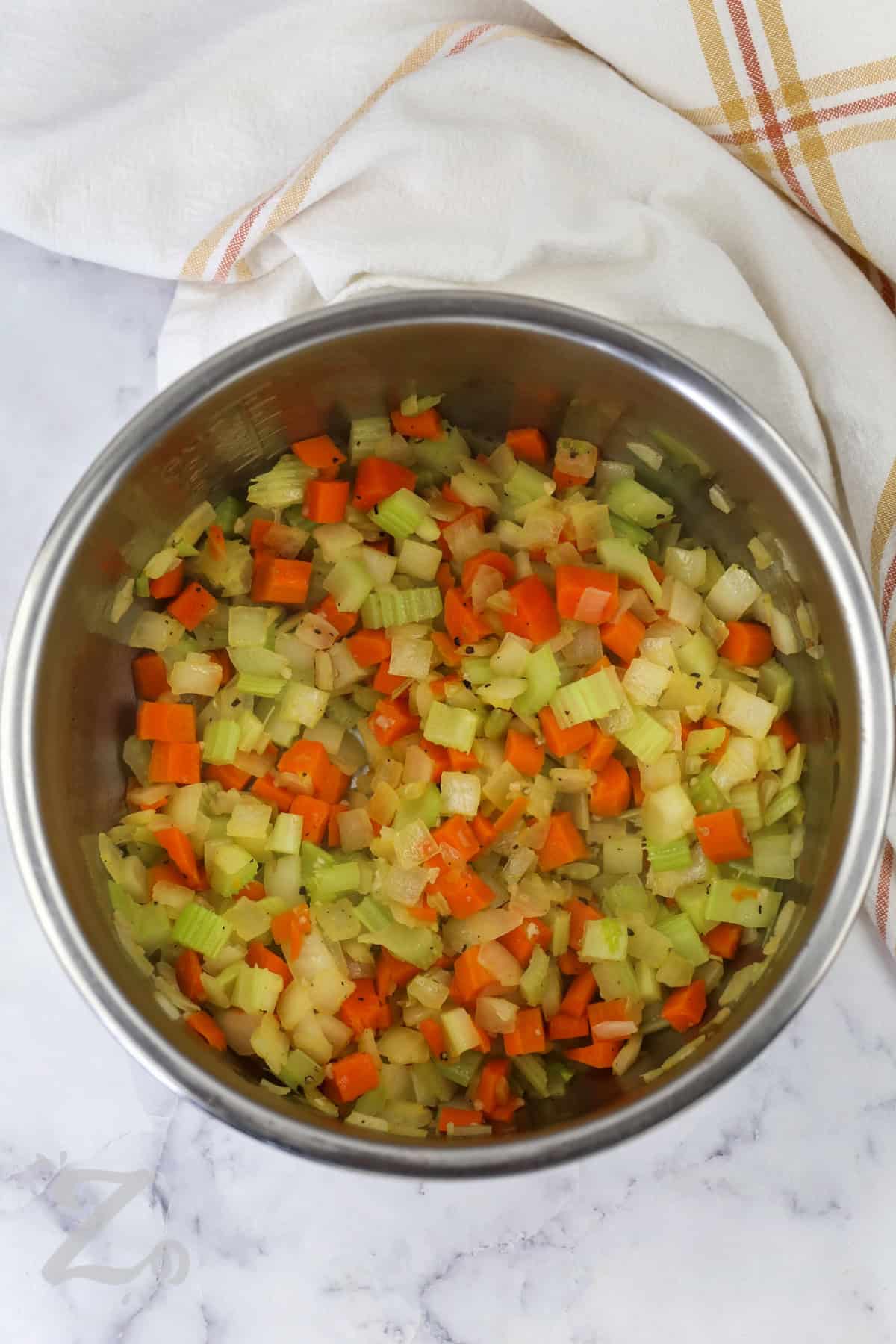 On cool evenings, Instant Pot split pea soup makes the perfect warm and filling dinner. Smoky ham and creamy split peas blend with carrots, celery, and herbs to create a rich homemade soup recipe everyone will love. This hearty pressure cooker meal tastes comforting and satisfying while using simple ingredients already in your pantry. It is the kind of family dinner recipe that keeps everyone coming back for seconds. Make this cozy soup recipe tonight. #ourzestylife cooked onion , carrots and celery with salt and pepper in a bowl to make Instant Pot Split Pea Soup with Ham