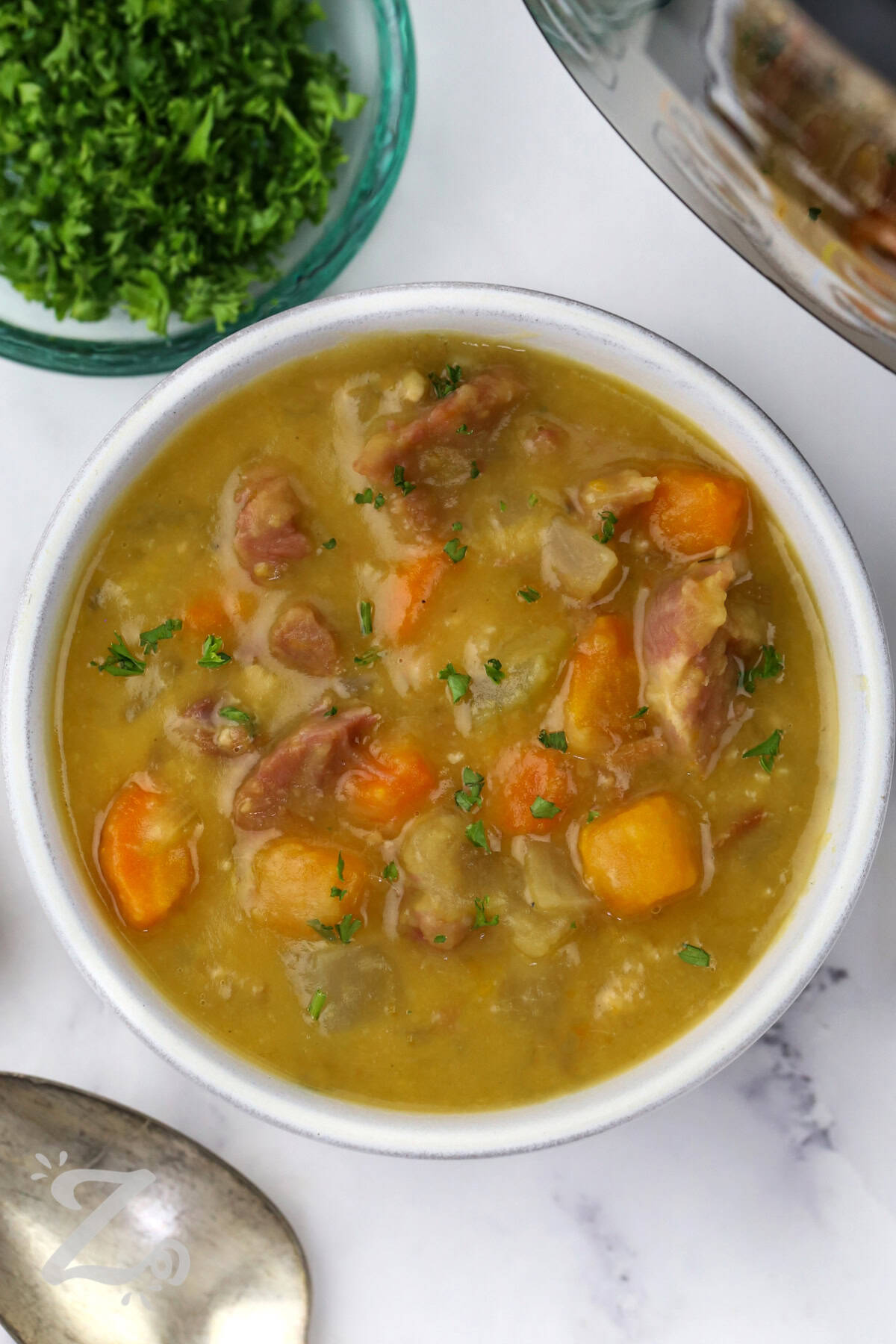 A bowl of Instant Pot split pea soup is the perfect way to warm up after a busy day. Smoky ham and creamy split peas create rich, savory flavor, while tender vegetables make every spoonful hearty and satisfying. This homemade pressure cooker soup recipe is easy to prepare and tastes like classic comfort food. It is budget-friendly, filling, and perfect for feeding a hungry family on cooler nights. Make this family favorite for dinner tonight. #ourzestylife plated dish of Instant Pot Split Pea Soup with Ham