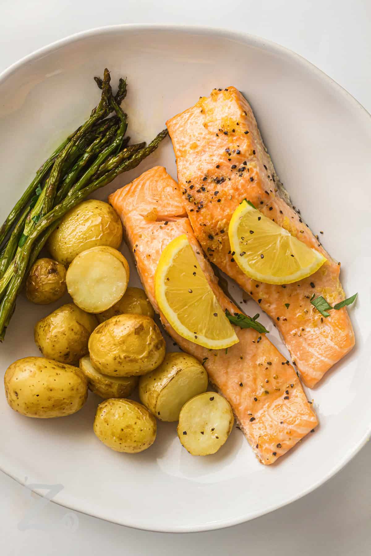 For busy evenings, sheet pan salmon is the kind of recipe that makes dinnertime easier. Everything cooks together in one pan, from the tender potatoes to the flavorful asparagus and salmon. The lemon garlic butter adds a fresh finish that brings the whole meal together. It is a healthy dinner option that the whole family can enjoy. Try it for dinner this week. #ourzestylife Sheet Pan Salmon with Asparagus and Roasted Potatoes on a plate with lemon slices