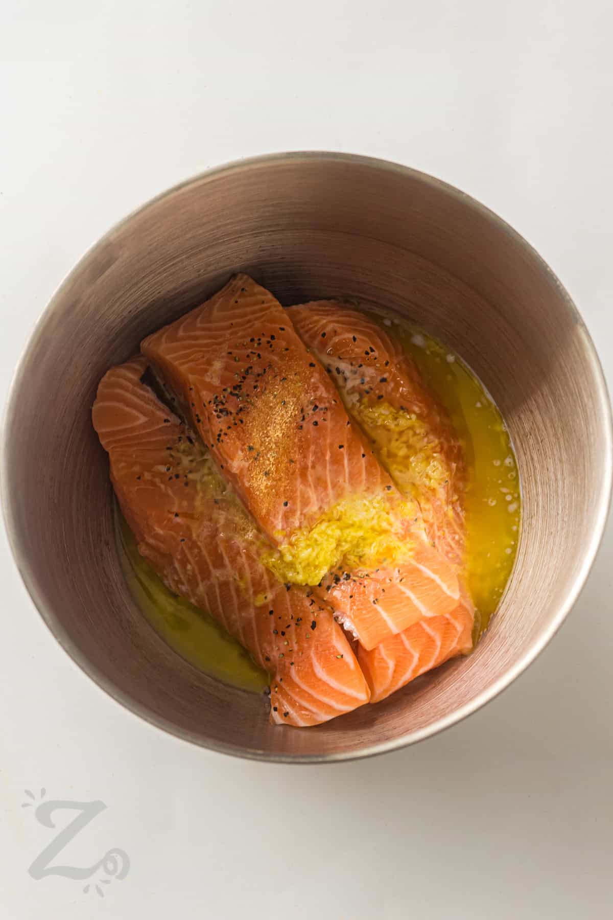 Sheet pan salmon is a fresh and flavorful dinner that delivers big results with simple ingredients. Flaky salmon fillets roast alongside potatoes and asparagus while a lemon garlic butter mixture adds bright, savory flavor. It is a complete meal that comes together easily and leaves fewer dishes behind. Try this healthy sheet pan dinner for your next family meal. #ourzestylife adding lemon and seasonings to salmon to make Sheet Pan Salmon with Asparagus and Roasted Potatoes