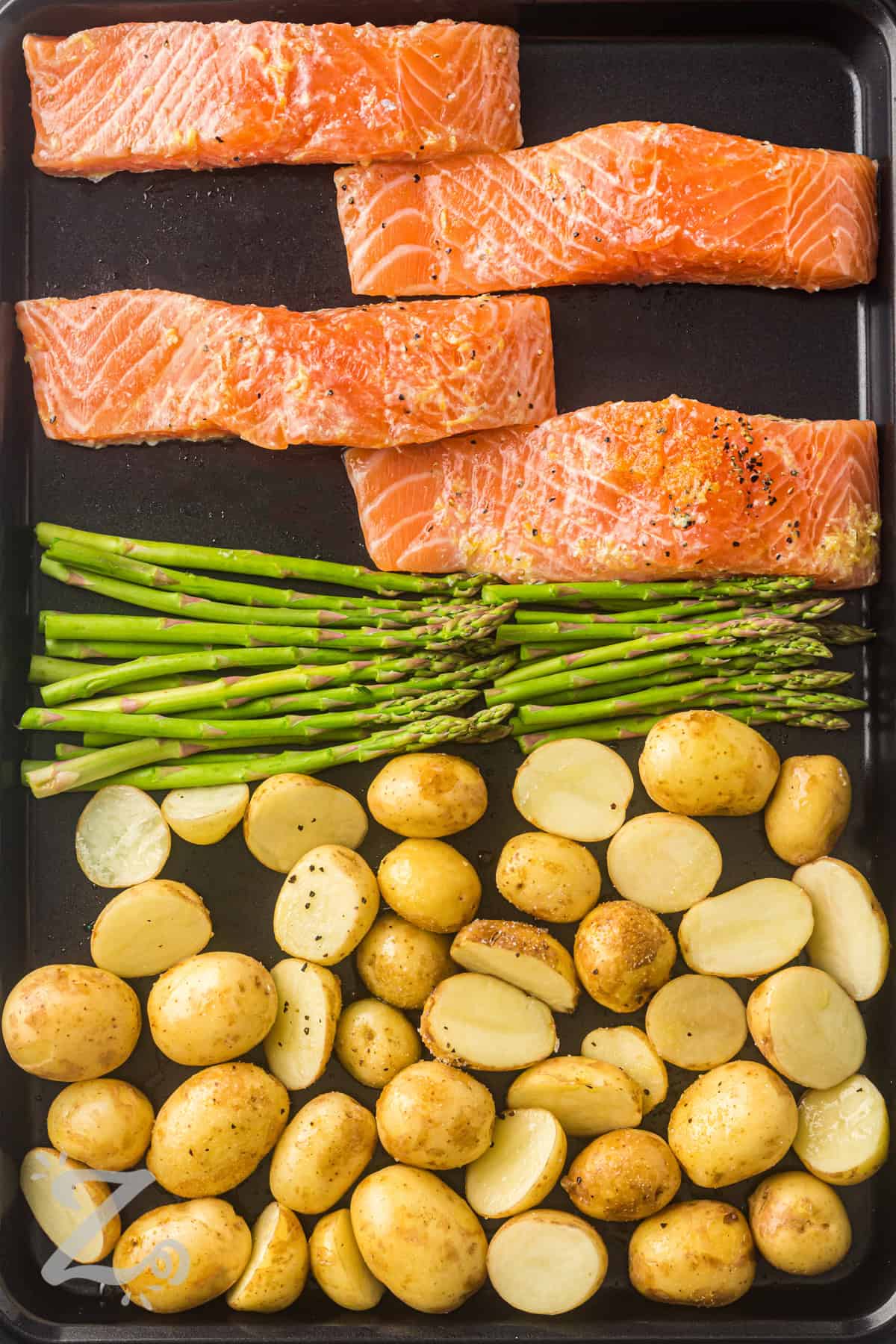 Sheet pan salmon makes dinner easy with flaky salmon, roasted potatoes, and fresh asparagus all cooked together on one pan. Bright lemon and garlic add fresh flavor to every bite, while the simple prep keeps cleanup to a minimum. This healthy salmon recipe is perfect for busy weeknights when you want a complete meal without extra work. Add this easy family dinner to your meal plan tonight. #ourzestylife adding ingredients to sheet pan to make Sheet Pan Salmon with Asparagus and Roasted Potatoes