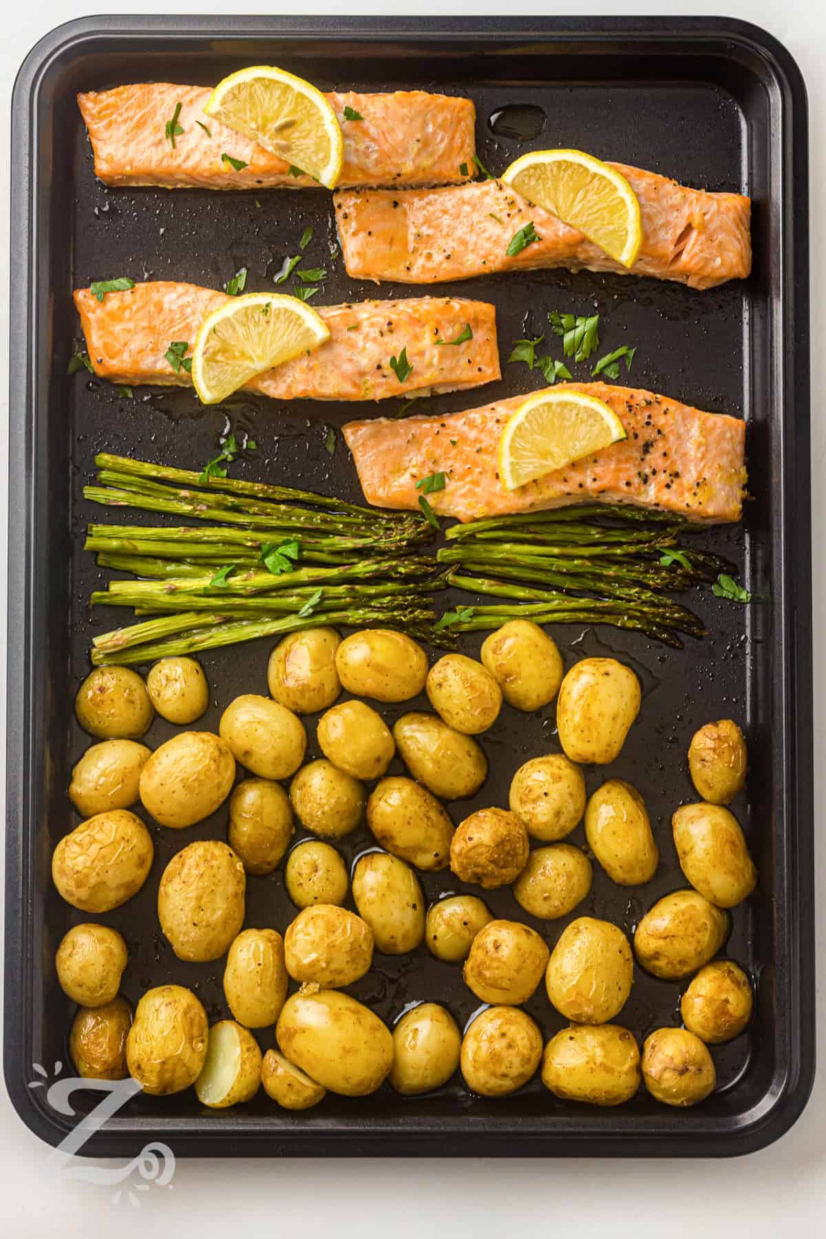 Sheet pan salmon is a healthy dinner recipe that keeps both cooking and cleanup simple. Tender potatoes roast until golden, while asparagus and salmon finish cooking together in the same pan. Fresh lemon and garlic add flavor without overpowering the natural taste of the ingredients. Add this easy weeknight meal to your regular dinner rotation. #ourzestylife sheet pan with Sheet Pan Salmon with Asparagus and Roasted Potatoes and lemon slices