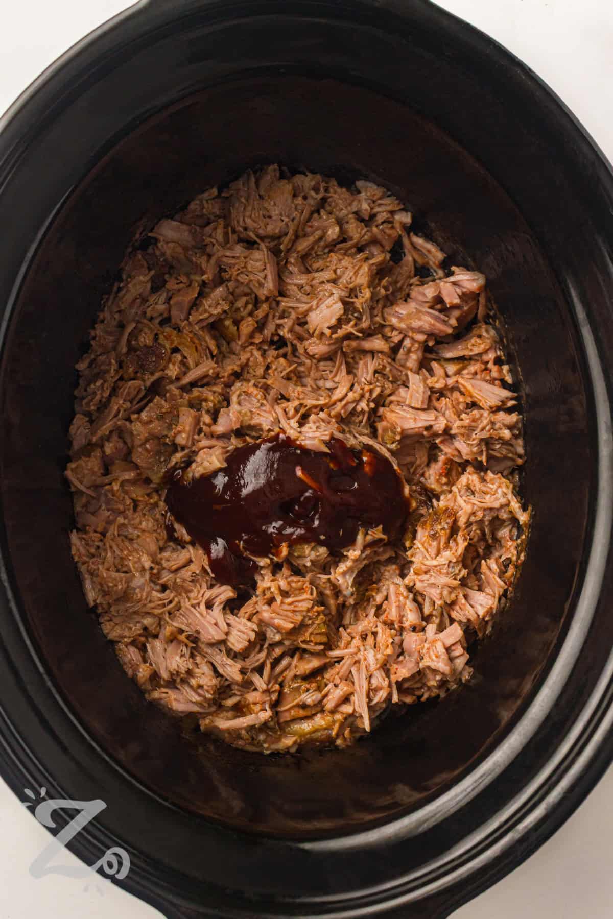 adding sauce to pulled pork to make Slow Cooker BBQ Pulled Pork