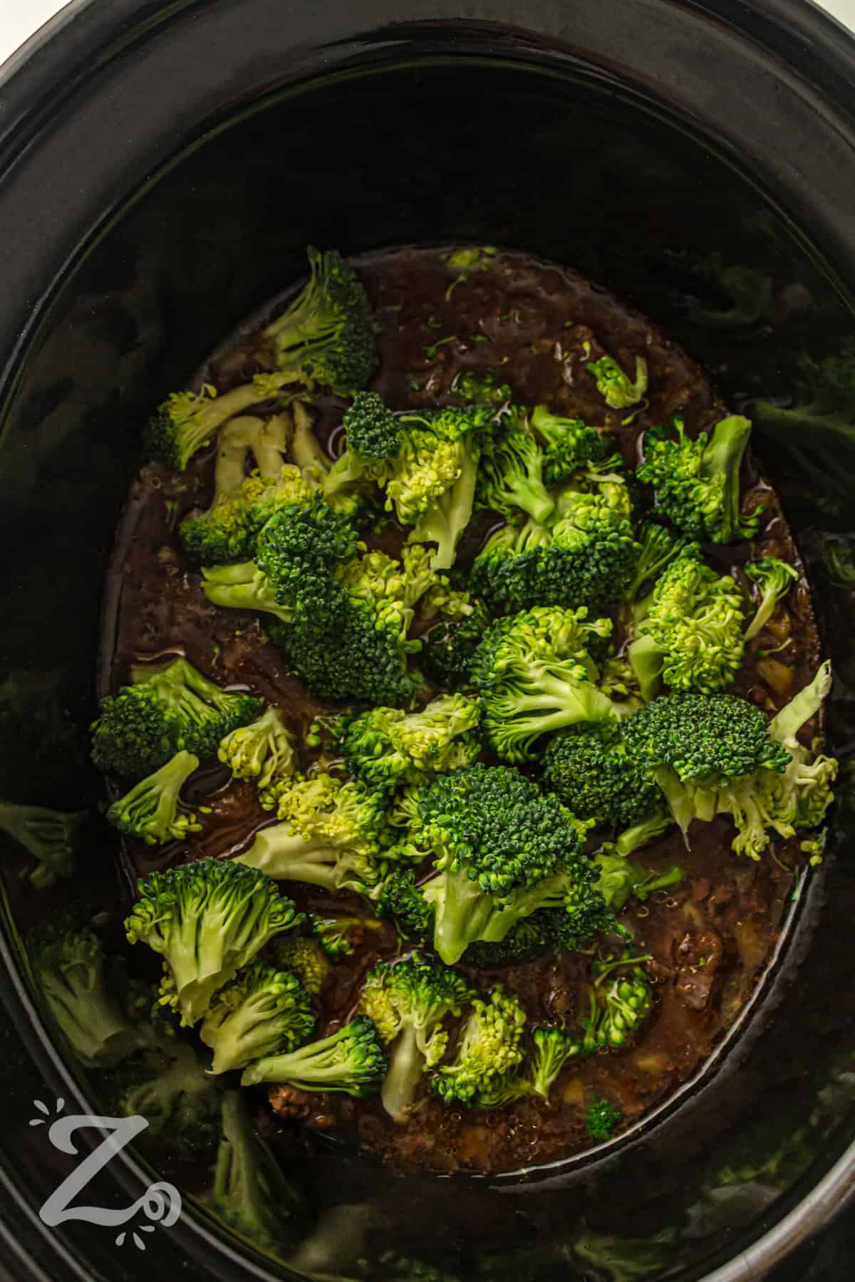 Slow cooker beef and broccoli makes dinner simple with a set it and forget it slow cooker recipe. It turns basic beef into a tender, flavorful dish coated in a savory Asian inspired sauce. Garlic and soy sauce create bold taste while broccoli adds fresh texture and color. This is a great option for easy weeknight meals or meal prep. Try it for a cozy homemade dinner and serve it with rice. #ourzestylife adding broccoli to pot to make Slow Cooker Beef and Broccoli