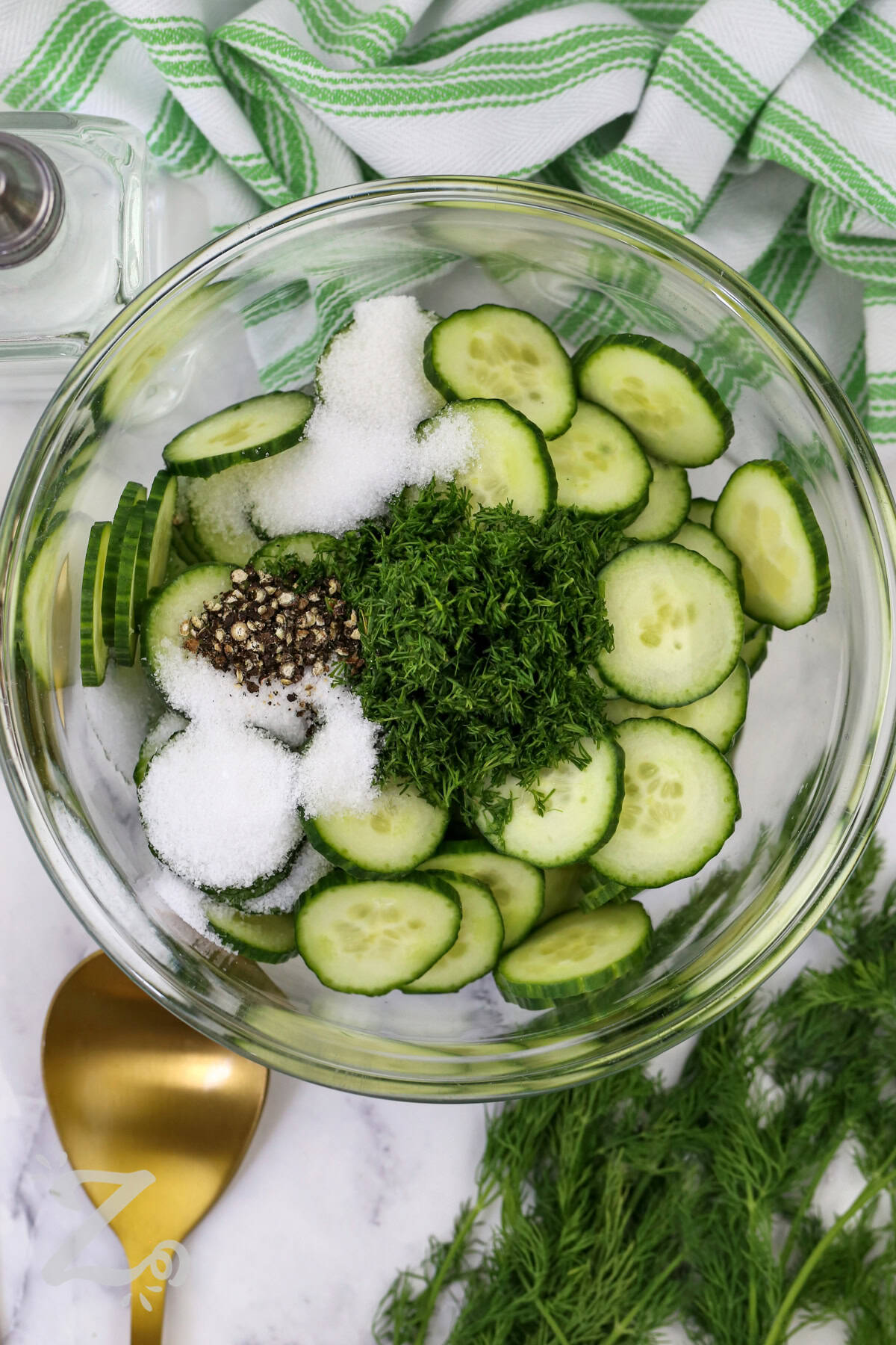 Fresh, easy cucumber salad is always a welcome addition to the table. English cucumbers, dill, and a simple vinegar dressing create a cool and flavorful side that complements almost any meal. It is an excellent choice for summer entertaining, potlucks, or everyday family dinners with fresh seasonal ingredients. Make this recipe and enjoy every bite. #ourzestylife adding ingredients together to make Easy Cucumber Salad