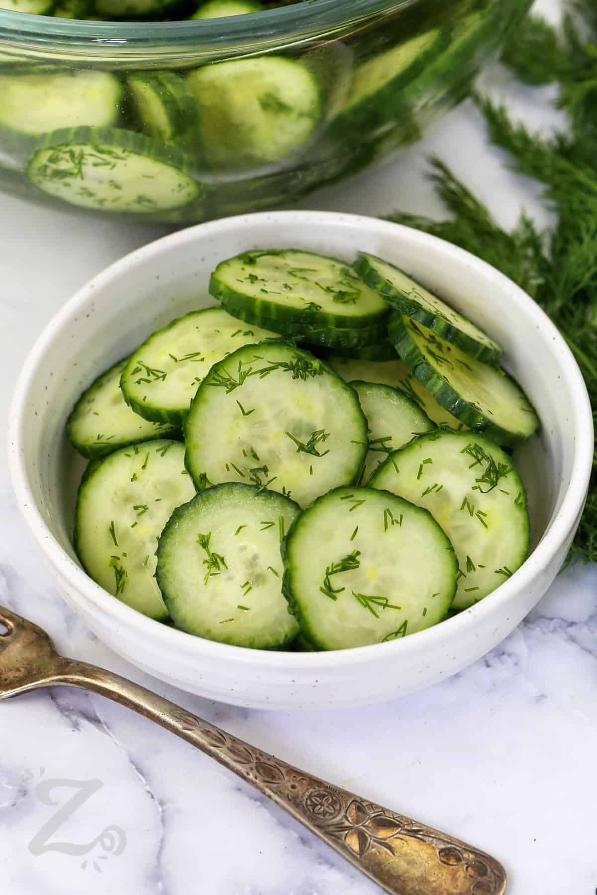 Here is an easy cucumber salad that belongs at every summer gathering. Fresh English cucumbers, chopped dill, and a tangy white wine vinegar dressing create a simple salad that tastes clean and refreshing. It pairs well with grilled meats, sandwiches, seafood, and picnic favorites for any occasion. Save this recipe and enjoy it often. #ourzestylife bowl of Easy Cucumber Salad