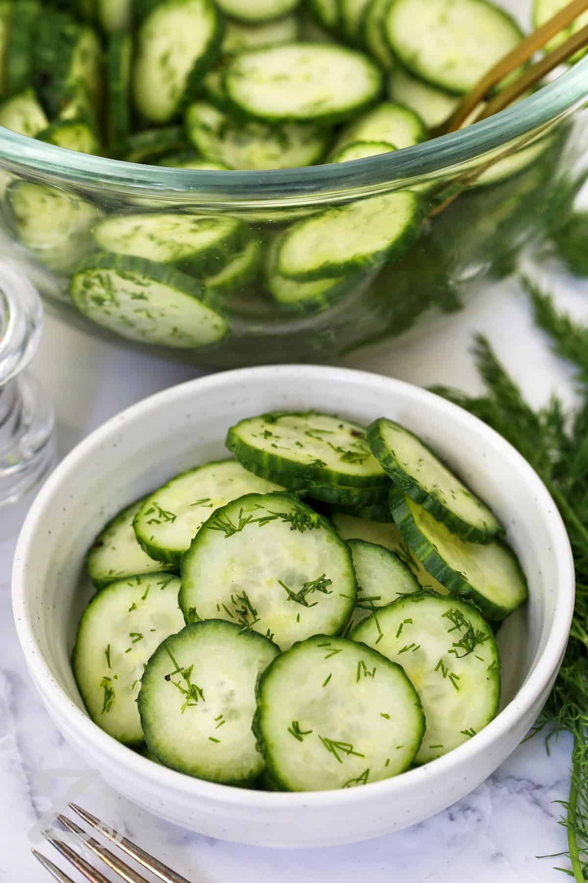 My easy cucumber salad is a simple way to enjoy fresh cucumbers at their best. The light dressing adds tangy flavor while fresh dill gives every bite a garden-fresh finish. This refreshing side dish is perfect for summer cookouts, family meals, and outdoor entertaining. Make this recipe and share it with friends. #ourzestylife plated Easy Cucumber Salad with a bowl full in the background