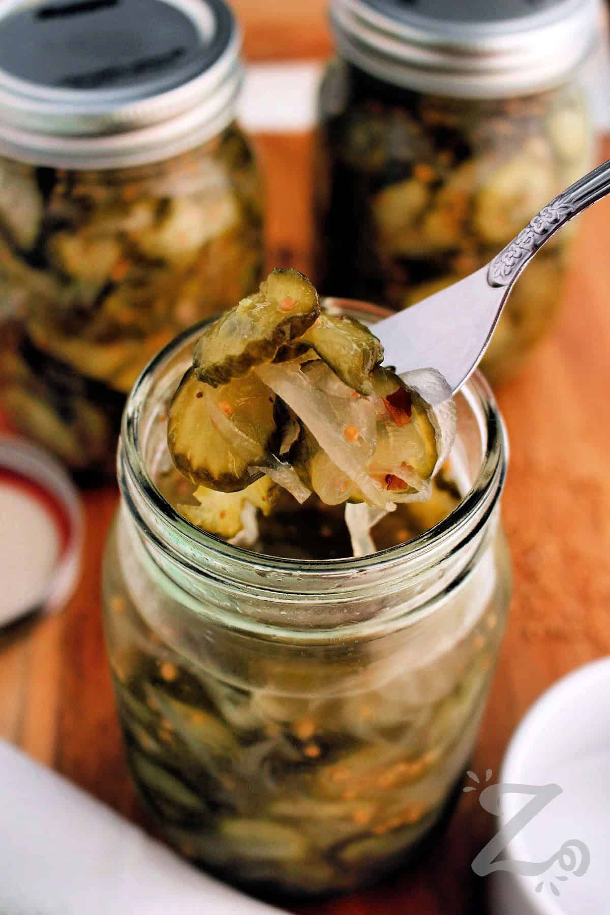 For an easy bread and butter pickles recipe, look no further? These homemade sweet pickles are packed with crisp cucumbers, onions, mustard seed, and a flavorful vinegar brine. It is a recipe you can use to can or make refrigerator pickles. Give it a try and you'll want to make it every summer. #ourzestylife completed bread and butter pickles recipe in a mason jar with some on a fork