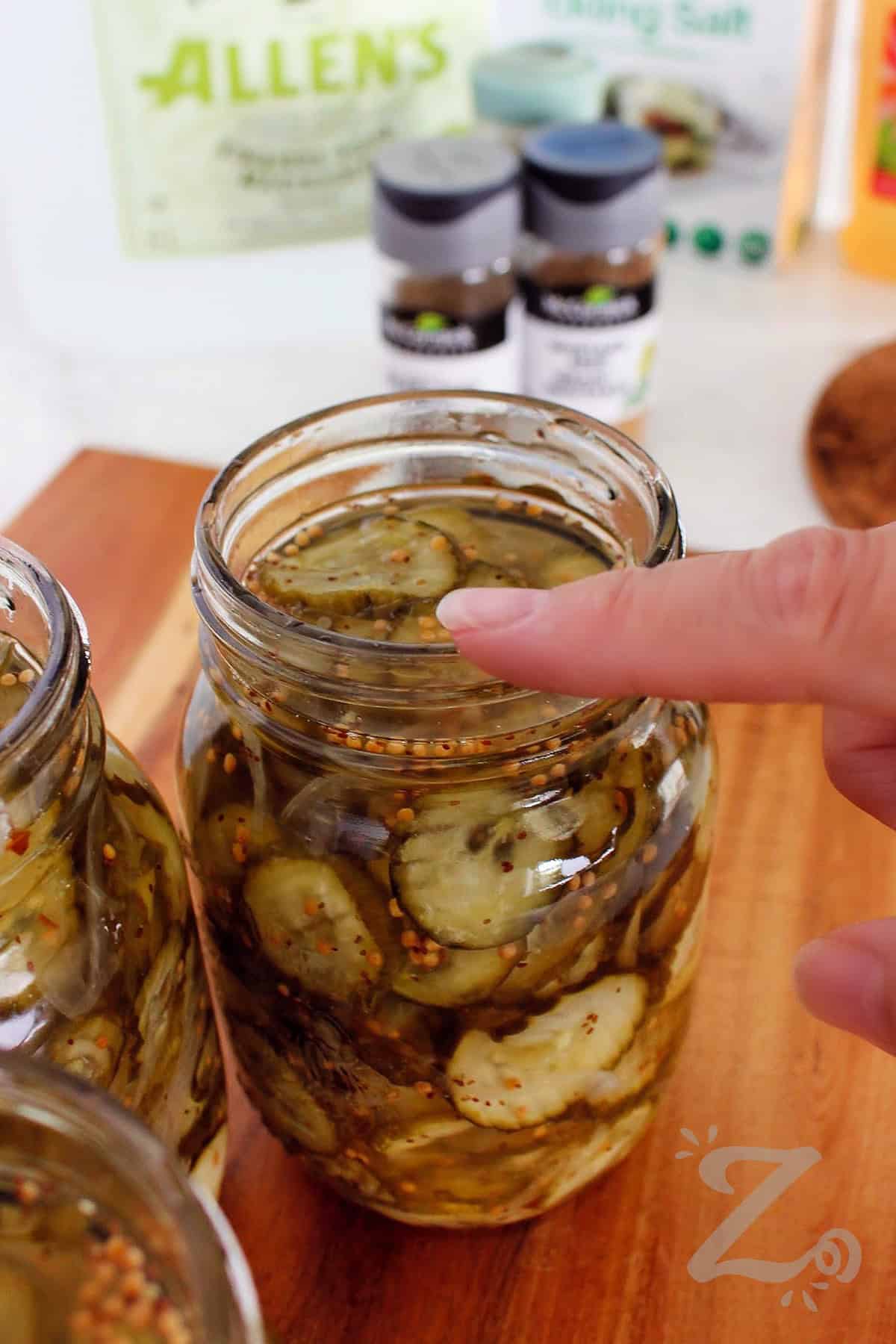 Looking for an easy Bread and Butter Pickles recipe to try at home this summer? Give this one a try and make a sweet and tangy treat everyone will enjoy. Using crisp cucumbers, onions, and a homemade brine you will create the perfect pickle for burgers, sandwiches, charcuterie boards, or snacking. Choose between canning or refrigerator style pickles! #ourzestylife process to make bread and butter pickles recipe checking the mason jar rim for any imperfections