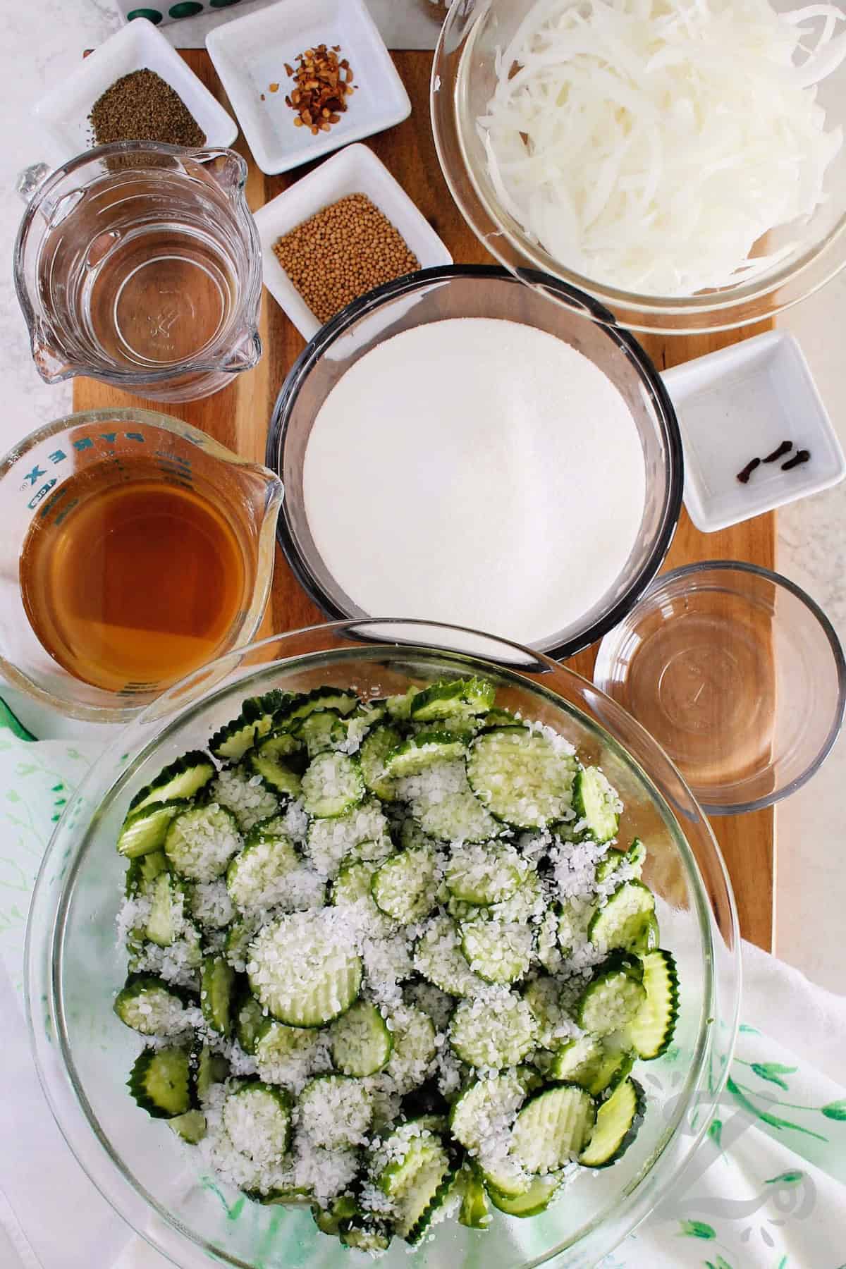 A batch of homemade pickles is easy to make with this bread and butter pickles recipe. It creates crisp, sweet pickles with just the right balance of vinegar, sugar, and spices. Create refrigerator pickles you can enjoy in 3 months time or water canned pickles to store for up to a year. Either way, this is a must try recipe. #ourzestylife process to make bread and butter pickles recipe with pickling salt added to sliced cucumbers