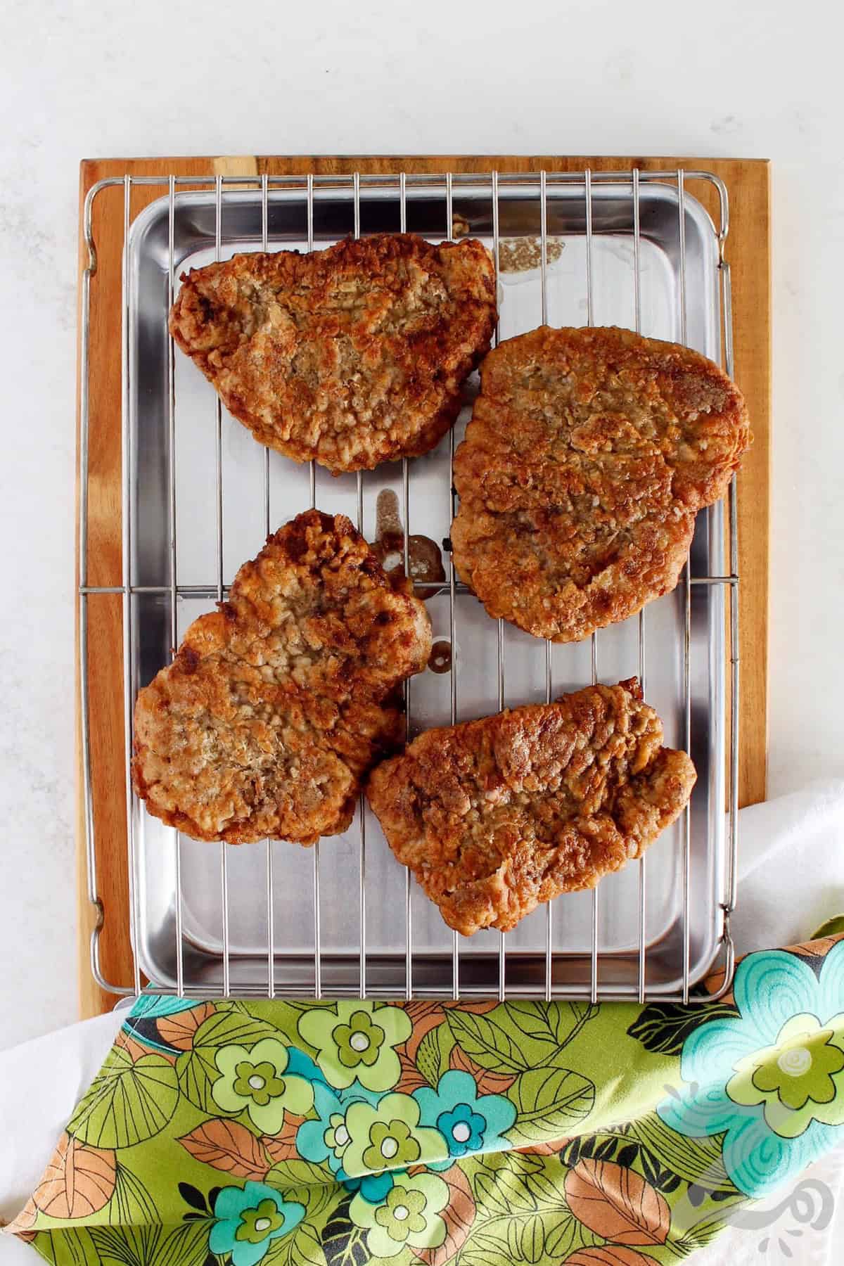 chicken fried steak after it has been fried, sitting on a wire rack