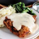 chicken fried steak with country gravy on a white plate with mashed potatoes and green beans on the side