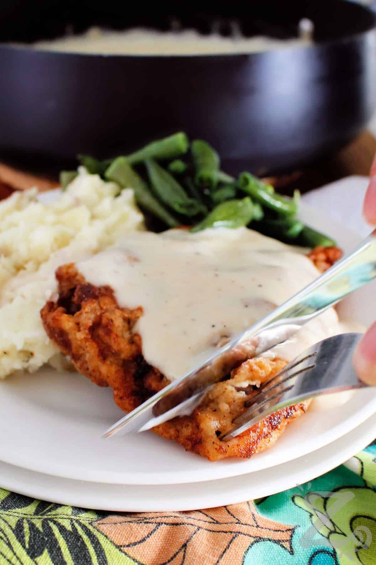chicken fried steak with country gravy with a knife and fork slicing off a bite sized piece