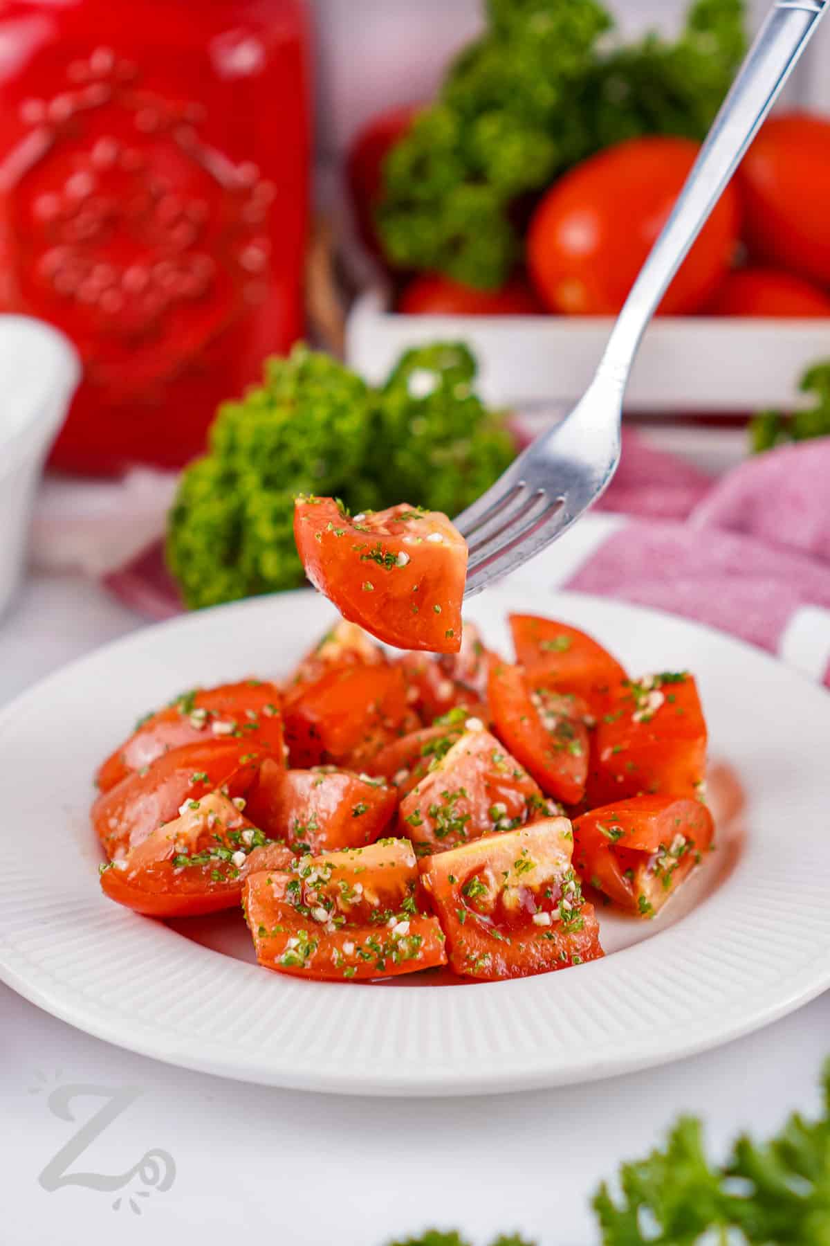 Marinated tomatoes are a fresh and flavorful side made with juicy Roma tomatoes, garlic, parsley, lemon, and olive oil. The simple marinade adds a bright, zesty flavor while letting the tomatoes shine. Serve them with grilled chicken, fish, pasta, or warm bread for an easy summer meal. Keep this fresh tomato recipe handy and give it a try. #ourzestylife plate full of Marinated Tomatoes with one on a fork