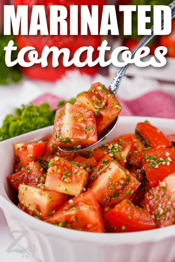 Marinated tomatoes are a fresh and flavorful way to enjoy ripe summer tomatoes. Roma tomatoes soak up a simple blend of olive oil, lemon juice, garlic, parsley, and salt for a bright side dish that pairs with almost any meal. They are delicious served with grilled meats, sandwiches, pasta, or toasted bread. Add this easy tomato recipe to your summer menu and give it a try. #ourzestylife dish of Marinated Tomatoes with some on a spoon and a title