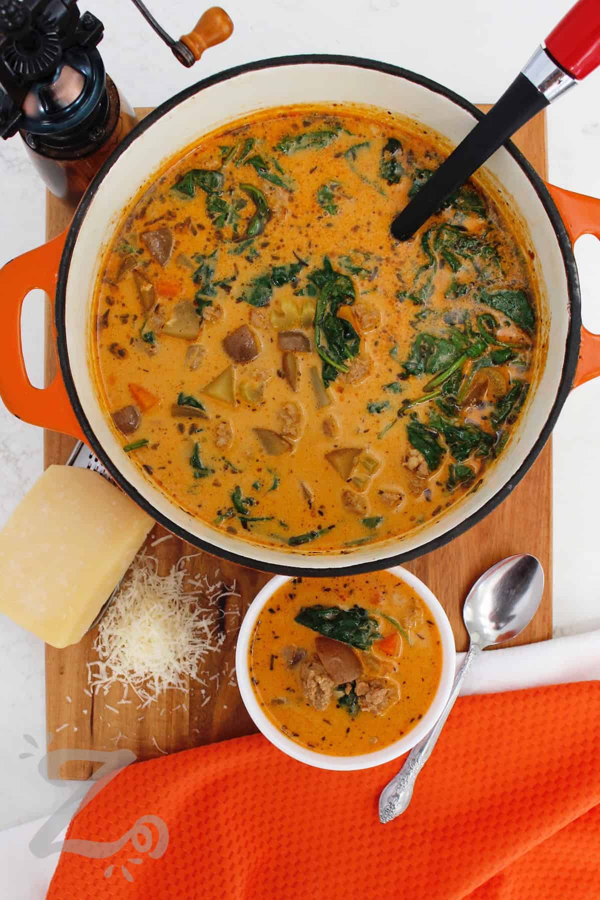 Easy, creamy, and satisfying, this Sausage Potato Soup is comfort food made simple. Italian sausage, potatoes, carrots, celery, and spinach simmer together in one pot before being finished with cream and Parmesan cheese. This flavorful soup is perfect for a family weeknight dinner. Why not make a pot and enjoy it tonight? #ourzestylife sausage potato soup in a pot with a bowl of soup and freshly shredded parmesan on the side.
