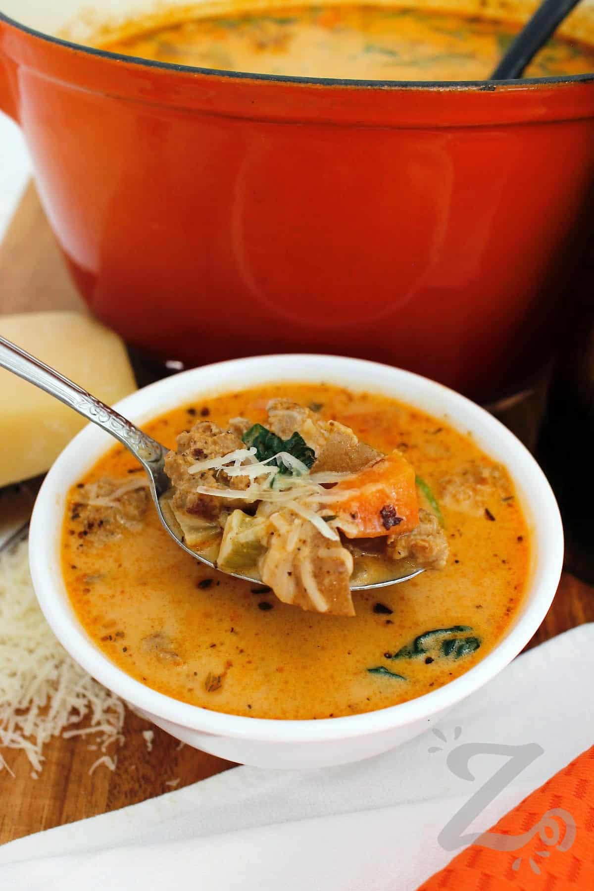 Create a cozy meal for your family with this Sausage Potato Soup recipe. Italian sausage, tender potatoes, carrots, celery, and spinach, are prepared in a zesty broth finished with cream. A touch of red pepper adds just enough heat to balance the rich, savory flavors. Enjoy this hearty soup that is perfect for a chilly weeknight meal so why not make a pot tonight? #ourzestylife a spoon filled with sausage potato soup in a white bowl.