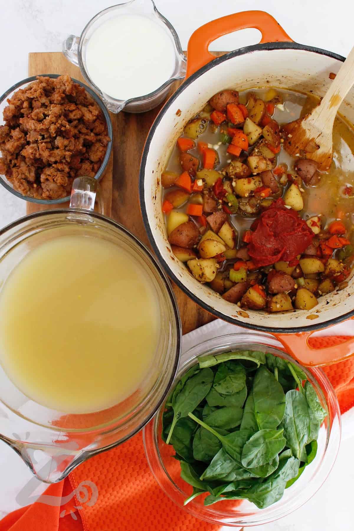 This creamy Sausage Potato Soup is an easy one pot meal that brings plenty of flavor to the table. Italian sausage, red potatoes, carrots, celery, garlic, herbs, and spinach are finished with rich cream and optional Parmesan cheese. Every spoonful is hearty and comforting, so try this easy dinner soon! #ourzestylife process to make sausage potato soup when broth and tomato paste have been added.