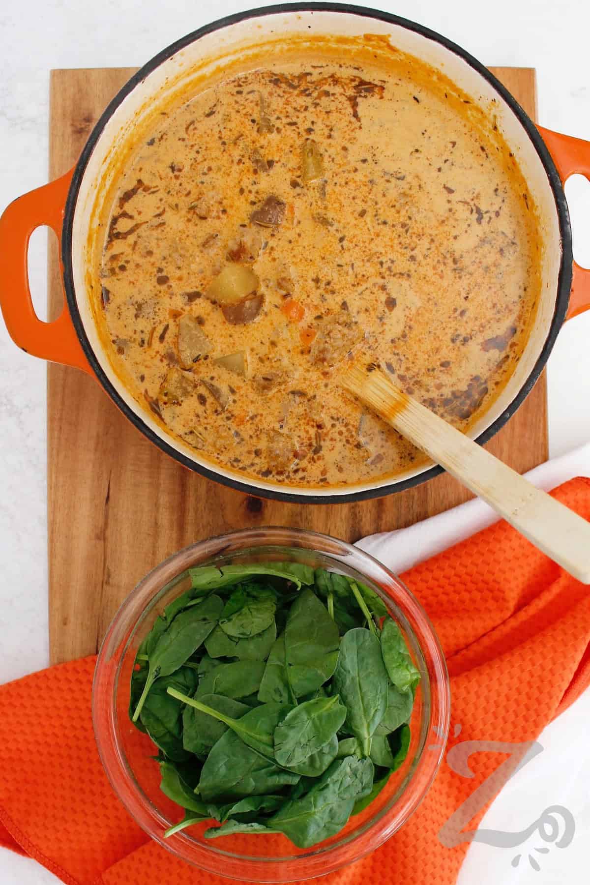 Craving a creamy soup with plenty of savory flavor? This Sausage Potato Soup is loaded with Italian sausage, tender potatoes, vegetables, and spinach. The rich broth has a hint of tomato, Italian seasoning, and just enough red pepper heat. This soup makes an easy cold weather dinner. Why not put it on the menu? #ourzestylife sausage potato soup in a pot with spinach in a clear bowl on the side.
