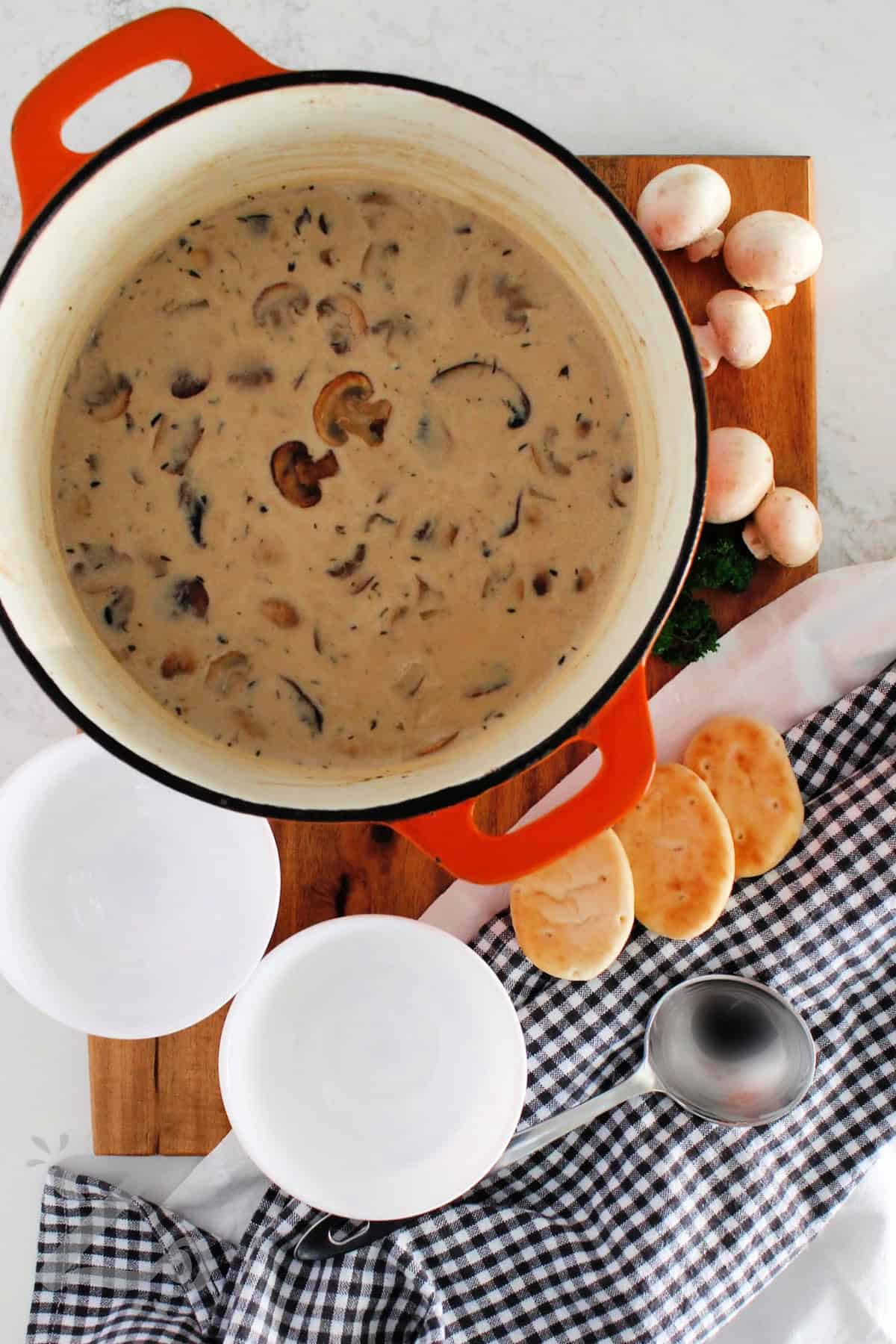 Homemade cream of mushroom soup in a pot with white bowls, mushrooms and pitas on the side.