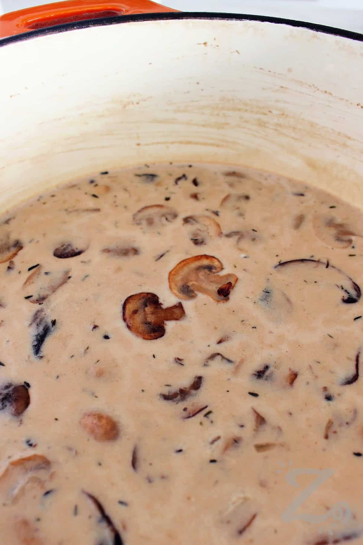 A pot filled with homemade cream of mushroom soup garnished with mushrooms.