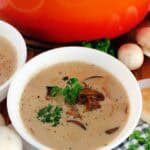 Homemade cream of mushroom soup garnished with fresh parsley, mushrooms, and freshly ground pepper.