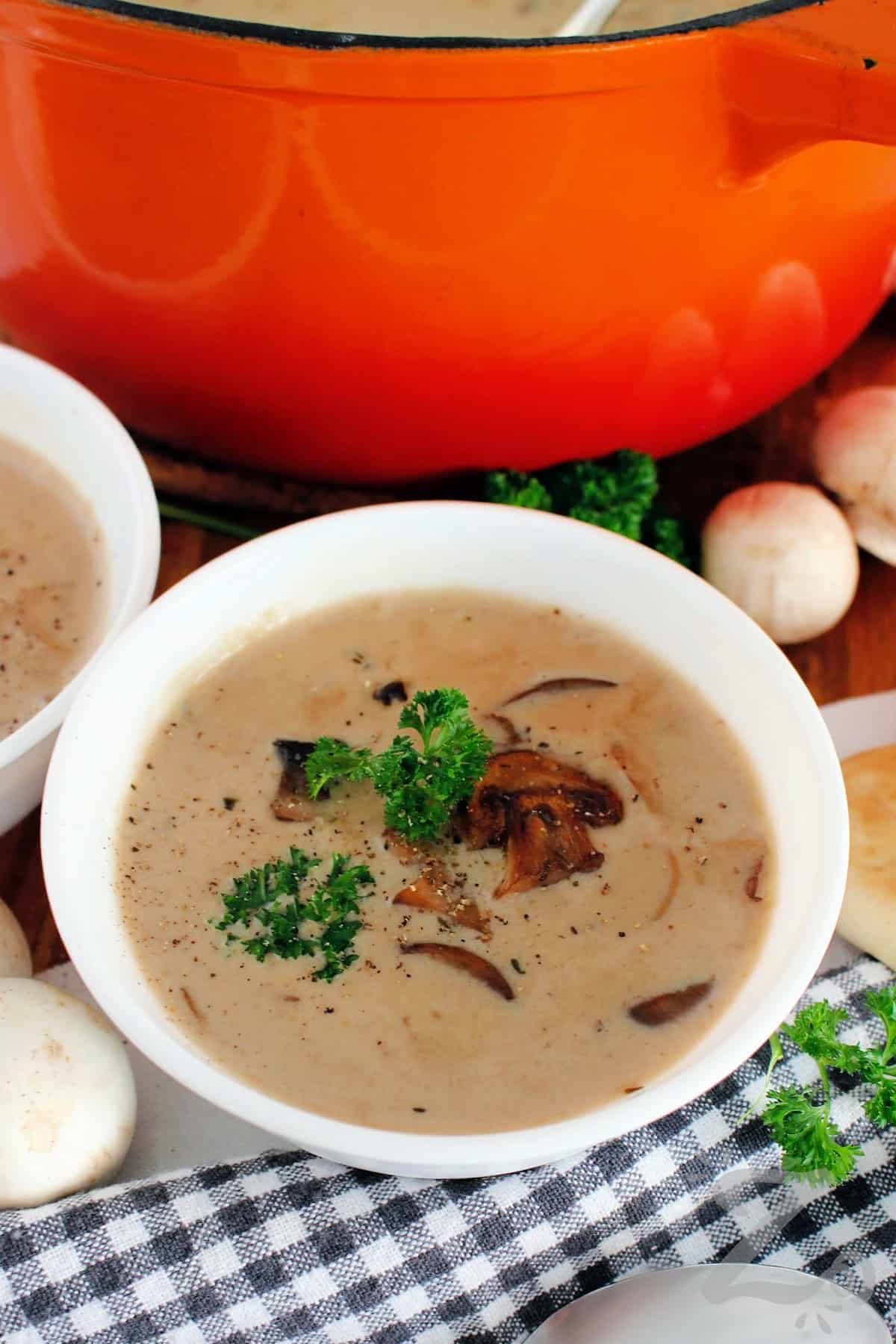Homemade cream of mushroom soup garnished with fresh parsley, mushrooms, and freshly ground pepper.