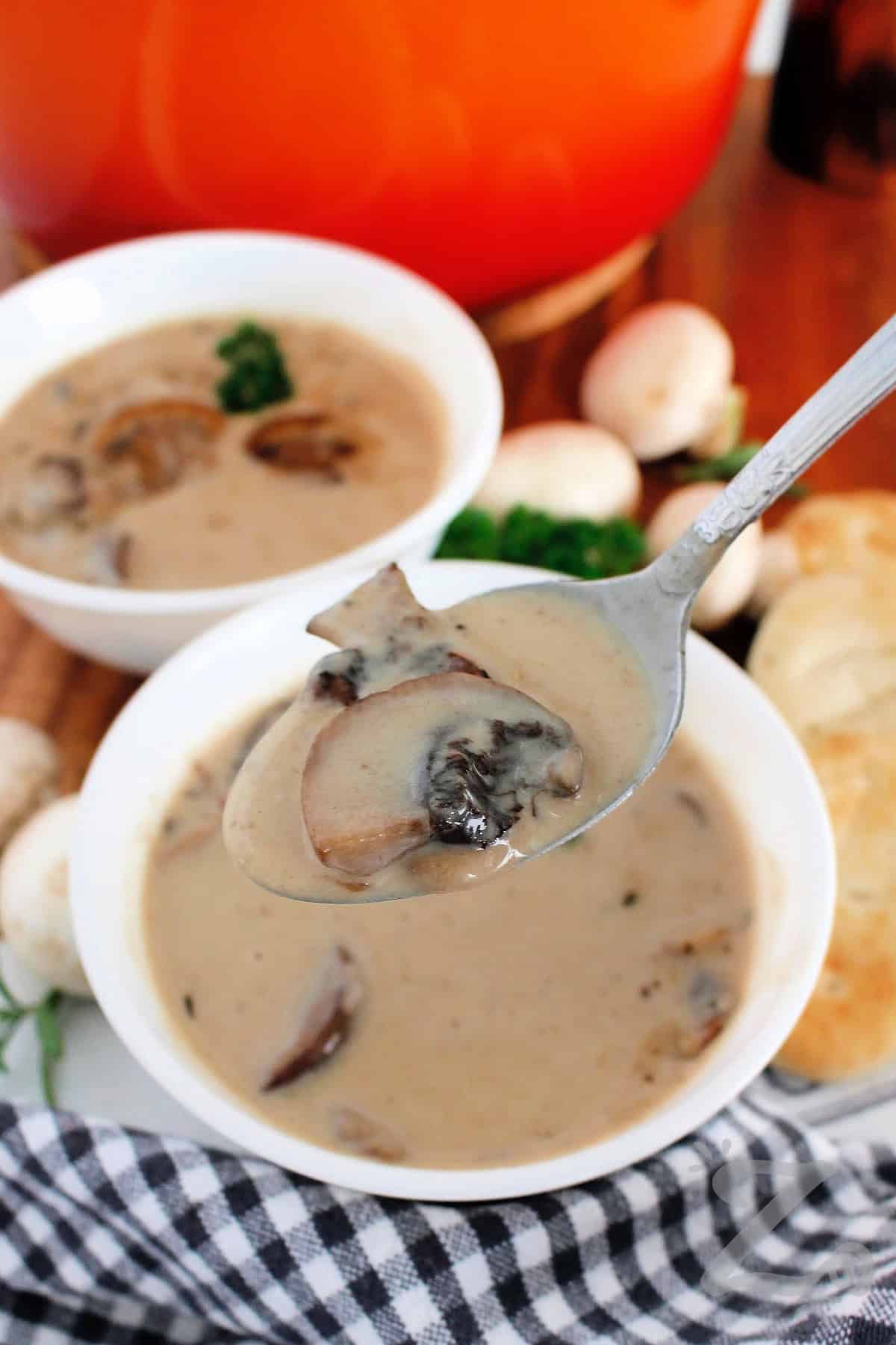 A spoon full of homemade cream of mushroom soup, with two bowls of it in the background.