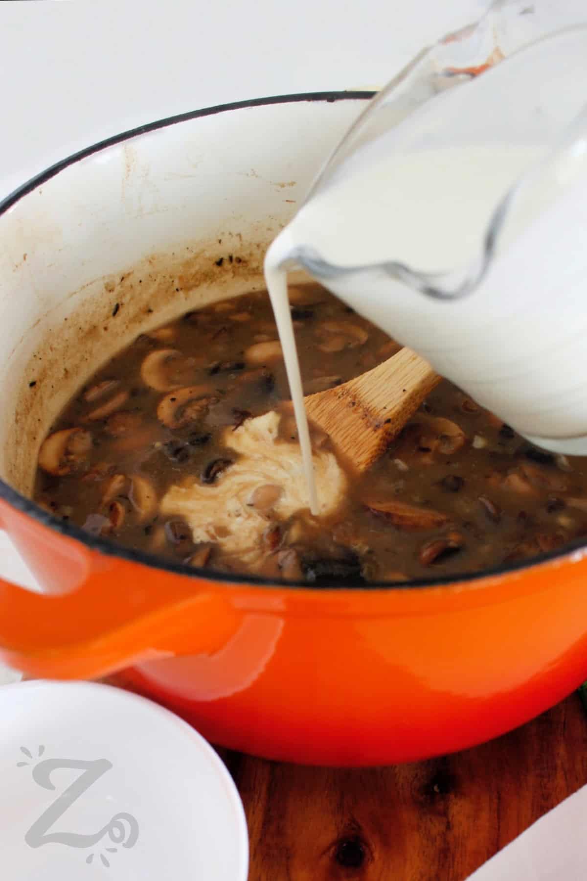 Pouring cream into a pot of homemade cream of mushroom soup.